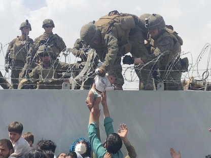 جندي من مشاة البحرية الأميركية يحمل رضيعاً فوق سياج من الأسلاك الشائكة أثناء عملية إجلاء في مطار حامد كرزاي الدولي، كابول، أفغانستان - 19 أغسطس 2021. - AFP