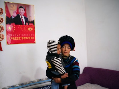 أمرأة وطفلها قرب صورة للرئيس الصيني شي جين بينغ في منزلها الجديد بمقاطعة سيشوان - 10 سبتمبر 2020 - REUTERS
