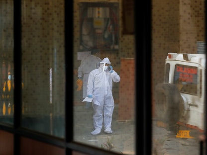شخص يرتدي بدلة واقية يقف بجانب سيارة إسعاف تحمل أحد أفراد أسرته الذي توفي بسبب فيروس كورونا  في نيودلهي بالهند - 24 أبريل 2021 - REUTERS