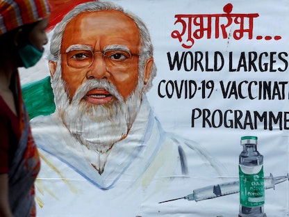  امرأة تمر أمام لوحة لرئيس الوزراء الهندي ناريندرا مودي قبل يوم من افتتاح حملة التطعيم ضد فيروس كورونا في مومباي، 15 يناير 2021. - REUTERS