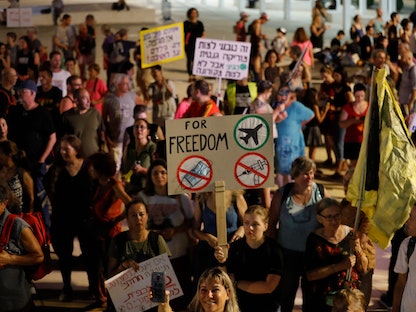 محتجون إسرائيليون يرفعون لافتات في مسيرة تندد بالقيود الحكومية الجديدة لمكافحة جائحة كورونا في تل أبيب - AFP