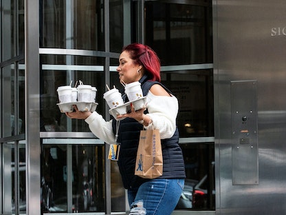 موظفة تحمل أكواباً من القهوة أمام مقر بنك في نيويورك، الولايات المتحدة. 12 مارس 2023 - REUTERS
