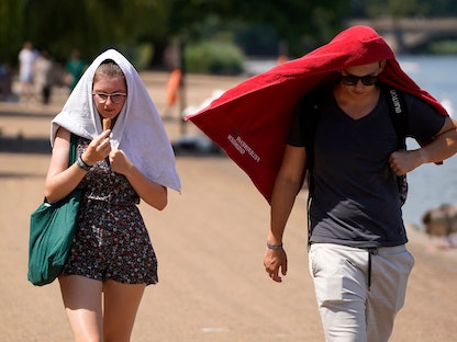 شخصان يحاولان الاحتماء من أشعة الشمس بأحد شوارع العاصمة البريطانية لندن تزامناً مع تسجيل درجة حرارة قياسية - 19 يوليو 2022 - AFP