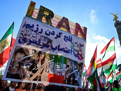متظاهرون يرفعون لافتة احتجاجية وأعلاماً إيرانية وكردية في مسيرة لدعم المظاهرات في إيران، برلين - 22 أكتوبر 2022 - AFP