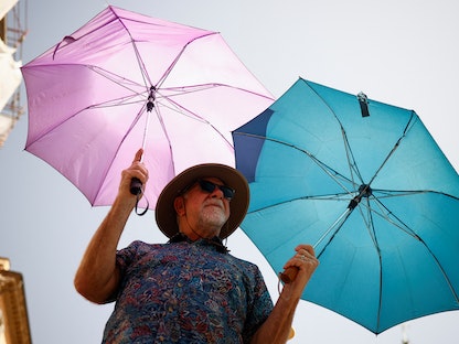 شخص في العاصمة الإيطالية روما يحمل مظلتين لاتقاء حرارة الشمس. 19 يوليو 2023 - REUTERS