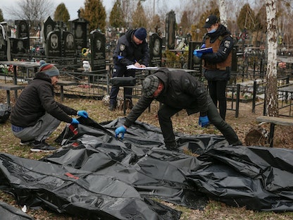 محققون أوكرانيون يتفحصون جثث مدنيين قضوا نحبهم في مدينة بوتشا- 6 أبريل 2022 - REUTERS