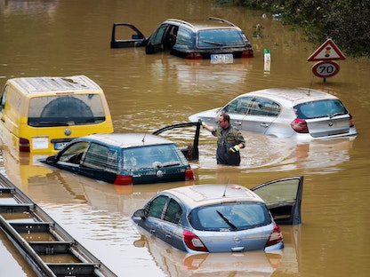 أحد أفراد قوات الجيش الألماني محاطاً بسيارات مغمورة جزئياً يخوض في مياه الفيضان بعد هطول أمطار غزيرة، 17 يوليو 2021 - REUTERS