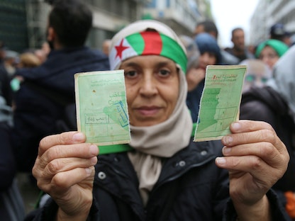 متظاهرة تحمل بطاقة تصويت خلال مظاهرات رافضة للانتخابات الرئاسية التي جرت في ديسمبر 2019  - REUTERS