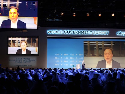 محمد القرقاوي وزير شؤون مجلس الوزراء الإماراتي (على خشبة المسرح) يتحدث مع إيلون ماسك عبر الفيديو خلال القمة العالمية للحكومات في دبي- 15 فبراير 2023 - AFP