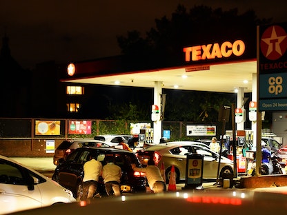 أشخاص يدفعون سيارة نفد وقودها قبل مسافة قصيرة من مضخات الوقود، بينما تنتظر السيارات لإعادة ملئها في محطة وقود في جنوب العاصمة البريطانية لندن، 26 سبتمبر 2021 - REUTERS