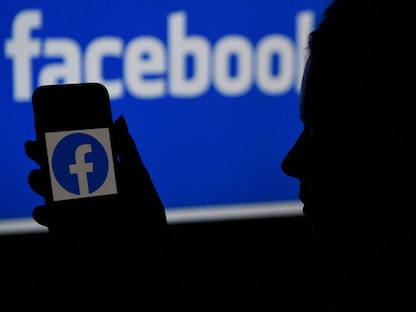 صورة مُركبة تتضمن شخصاً ينظر إلى شاشة هاتف ذكي تحمل شعار "فيسبوك" وفي الخلفية اسم شبكة التواصل - AFP