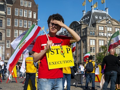 متظاهر يحمل لافتة وعلم إيران في ساحة دام في أمستردام، هولندا، للتنديد بإعدام المصارع الإيراني نافيد أفكاري - AFP