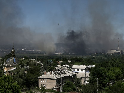 مبنى مدمر في ليسيتشانسك بينما يتصاعد الدخان من مدينة سيفيرودونيتسك القريبة جراء المعارك الدائرة بين القوات الروسية والأوكرانية في منطقة دونباس شرقي أوكرانيا. 9 يونيو 2022 - AFP
