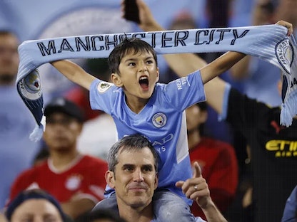 صبي على كتف والده يحمل وشاح نادي مانشستر سيتي في حماس خلال إحدى مباريات الدوري الإنجليزي - Reuters
