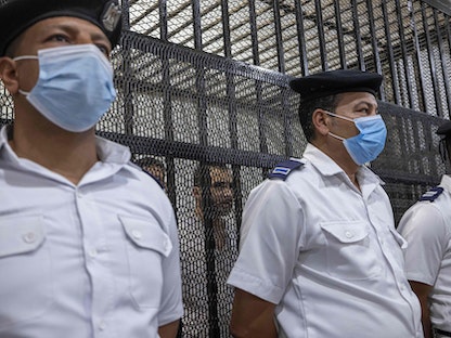 عدد من أفراد الشرطة المصرية أمام قفص الاتهام حيث يظهر طالب جامعة المنصورة المتهم بقتل زميلته "نيرة أشرف" - 26 يونيو 2022 - AFP