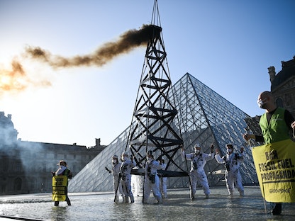 نشطاء منظمة "جرينبيس" يرتدون زي عمال البترول يقفون بجانب تمثال منشأة نفطية يتصاعد منها الدخان أمام هرم متحف اللوفر في باريس احتجاجاً على استمرار إنتاج الوقود الأحفوري واستهلاكه - 6 أكتوبر 2021 - AFP