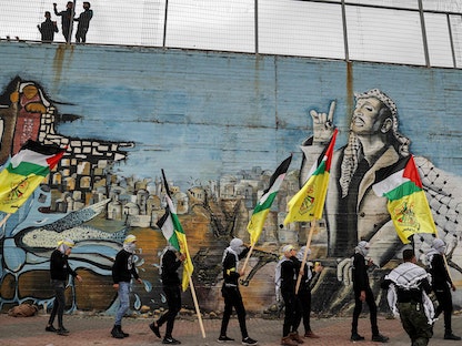ملثمون من حركة فتح يحملون أعلام الحركة مع أعلام فلسطين بجوار رسم جرافيتي للرئيس الفلسطيني الراحل ياسر عرفات في مدينة نابلس شمال الضفة الغربية المحتلة- 4 يناير 2022 - AFP