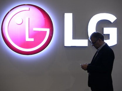 رجل ينظر في شاشة هاتفه خلال المرور أمام شعار شركة "إل جي- LG" في المؤتمر العالمي للجوال (MWC) ببرشلونة، إسبانيا، 26 فبراير 2019 - AFP