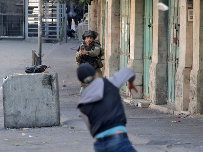 جندي إسرائيلي يصوب سلاحه تجاه شاب فلسطيني وسط مواجهات في مدينة الخليل بالضفة الغربية - 4 نوفمبر 2022 - AFP