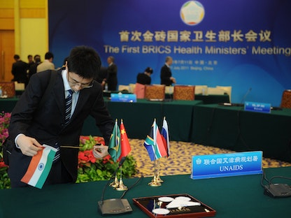 عنصر من اللجنة المنظمة لقمة بريكس يزيح أعلام دول المجموعة عقب انتهاء الاجتماع في العاصمة الصينية بكين- 11 يوليو 2011 - AFP