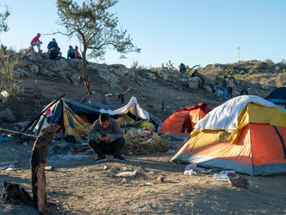 مهاجر صيني يجلس أمام خيمته بالقرب من السياج الحدودي بين الولايات المتحدة والمكسيك في كاليفورنيا. 6 ديسمبر 2023 - AFP