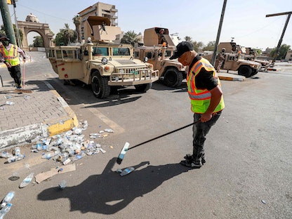 عمال البلدية ينظفون بينما ينتشر جنود من الجيش العراقي لحراسة مدخل المنطقة الخضراء شديدة الحراسة في العاصمة بغداد في 30 أغسطس 2022. - AFP
