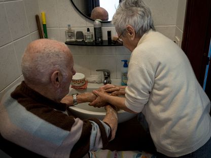 سيدة إيطالية تساعد زوجها (87 عاماً) الذي يعاني الخرف في غسل يديه  - via REUTERS