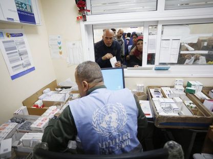 فلسطينيون ينتظرون أمام موظف تابع لوكالة غوث وتشغيل اللاجئين الفلسطينيين انتظاراً لصرف الدواء وسط أزمة في توافر المستحضرات الطبية، دير البلح، غزة. 21 يناير 2024 - AFP