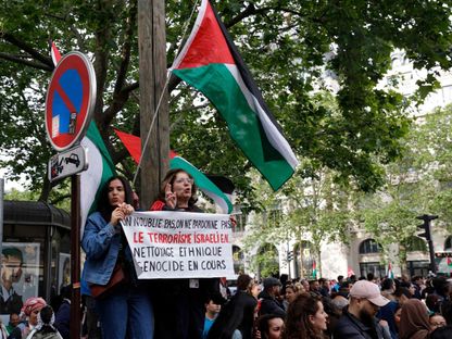 متظاهرتان ترفعان شعاراً مكتوب عليه "لن ننسى ولن نغفر للإرهاب الإسرائيلي. التطهير العرقي والإبادة الجماعية مستمرة" خلال تظاهرة في باريس احتجاجاً على الغارة الإسرائيلية على مخيم للنازحين في رفح. 27 مايو 2024 - AFP