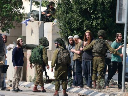 جنود إسرائيليون مع مستوطنين أمام مدخل قرية فلسطينية في الضفة الغربية المحتلة. 2 نوفمبر 2023 - AFP