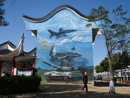رجل يمر أمام جدارية في منتزه عمومي تصور قطعاً عسكرية في جزيرة بينجتان، أقرب نقطة في الصين من الجزيرة الرئيسية لتايوان. منطقة فوجيان، الصين. 14 يناير 2024 - AFP