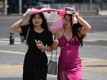 صينيتان تحتميان بسترة من أشعة الشمس في العاصمة الصينية بكين. 18 يونيو 2024 - AFP