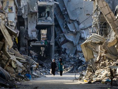 فلسطينيتان تسيران وسط مباني مدمرة جراء القصف الإسرائيلي على خان يونس، قطاع غزة. 20 يونيو 2024 - AFP