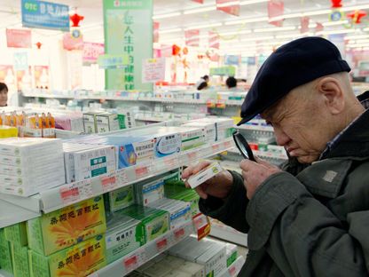 رجل مسن يستخدم عدسة مكبرة لقراءة تفاصيل علبة دواء في صيدلية بداندونغ في مقاطعة لياونينغ - REUTERS