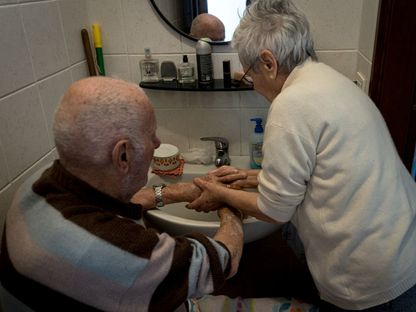صورة غير مؤرخة لسيدة إيطالية تساعد زوجها الذي يعاني من الخرف في غسل يديه - via REUTERS