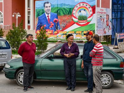 رجال يقفون يتحدثون أمام صورة الرئيس الطاجيكي إمام علي رحمون في قرية خوروسون بالقرب من أوبيكيك على بعد حوالي 70 كيلومتراً جنوب العاصمة دوشانبي. 26 مارس 2024 - AFP