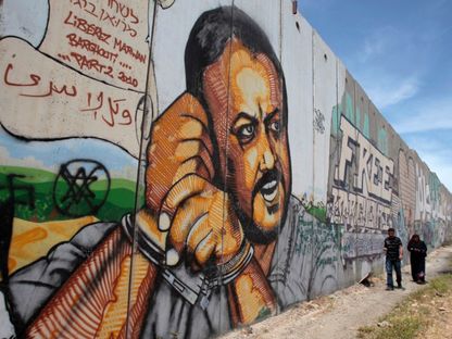 فلسطينيان يسيران قرب جدارية مرسومة لعضو اللجنة التنظيمية لحركة "فتح" مروان البرغوثي في رام الله. 25 مايو 2011 - REUTERS