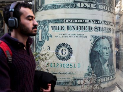شاب يمر أمام محل صرافة يعرض صورة للدولار الأميركي في أحد شوارع العاصمة المصرية القاهرة. 6 مارس 2024 - Reuters