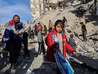فلسطينيون يسيرون بين أنقاض مبانٍ دمرتها الغارات الإسرائيلية في رفح جنوب قطاع غزة. 9 مارس 2024 - AFP