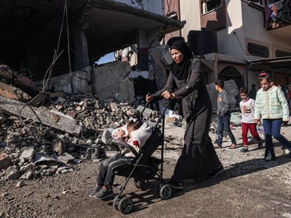 فلسطينيون يسيرون بجوار أنقاض مباني دمرتها غارات إسرائيلية في رفح، جنوب قطاع غزة. 24 فبراير 2024 - AFP
