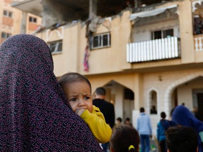 امرأة تحمل طفلاً تقف في موقع غارة إسرائيلية على مبنى سكني في خان يونس بجنوب قطاع غزة. 18 نوفمبر 2023 - Reuters