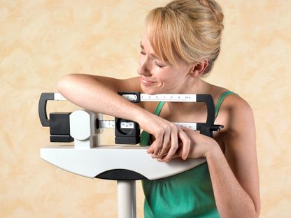امرأة متكئة على ميزان وتبدو غير راضية عن وزنها - Getty Images