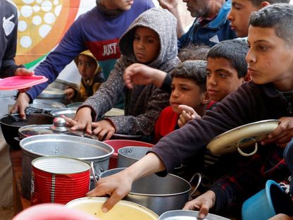 أطفال فلسطينيون ينتظرون الحصول على الطعام الذي أعدته جمعية خيرية، خلال شهر رمضان في خان يونس، جنوب قطاع غزة. 9 مارس 2025 - Reuters