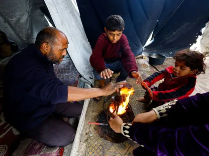 فلسطينيون يدفئون أيديهم داخل خيمة، في يوم ممطر بوسط قطاع غزة. 16 نوفمبر 2025 - REUTERS