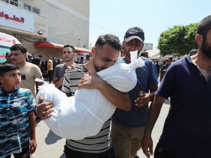 رجل فلسطيني يبكي حاملاً طفله الذي قتلته غارات إسرائيلية على دير البلح بوسط قطاع غزة. 27 يوليو 2024 - REUTERS