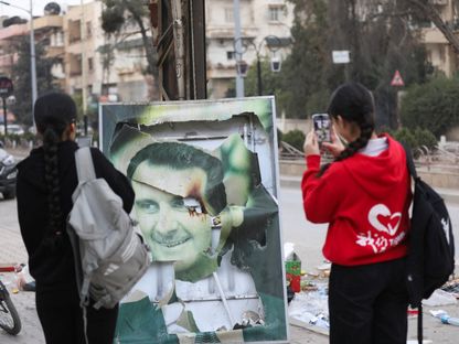 فتاتان سوريتان بالقرب من صورة متضررة للرئيس السوري بشار الأسد في القامشلي بسوريا. 8 ديسمبر 2024. - reuters