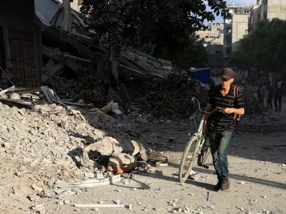 رجل فلسطيني يحمل دراجة هوائية في موقع غارة إسرائيلية استهدفت منزلاً خلال الليل في مدينة غزة. 7 أغسطس 2025 - Reuters