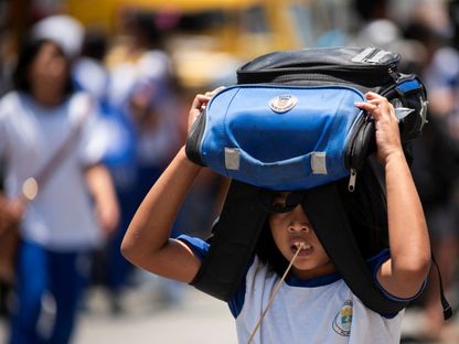 طالبة تستخدم حقيبتها المدرسية للاحتماء من أشعة الشمس خارج مدرسة في مانيلا بالفلبين. 19 أبريل 2024 - Reuters