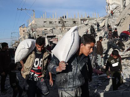 فلسطينيون يحملون بعض المساعدات بينما يتفقد آخرون أحد المنازل المدمرة جراء قصف إسرائيلي على رفح للبحث عن ناجين أو مصابين بين الأنقاض. 9 مارس 2024 - AFP