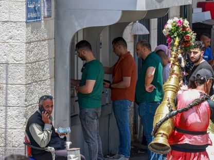 فلسطينيون يصطفون لسحب الأموال من جهاز صراف آلي في السوق الرئيسي بمدينة رام الله في الضفة الغربية التي تحتلها إسرائيل. 9 يونيو 2024 - AFP